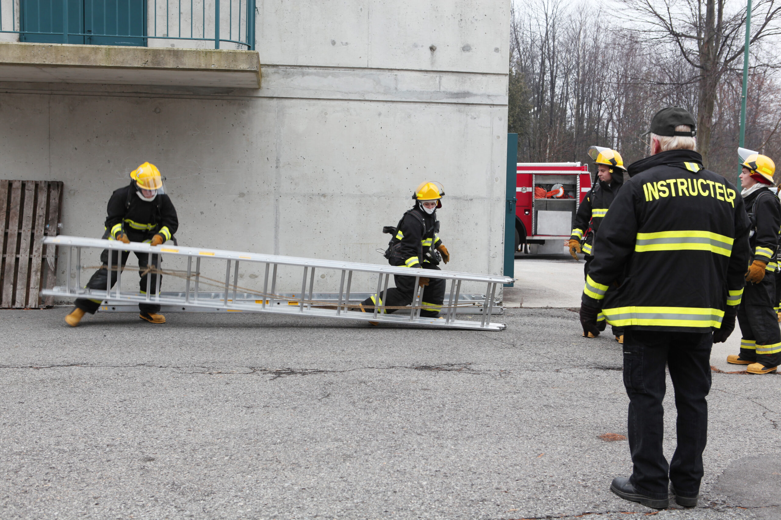 Fire Instructor training three firemen with a ladder.