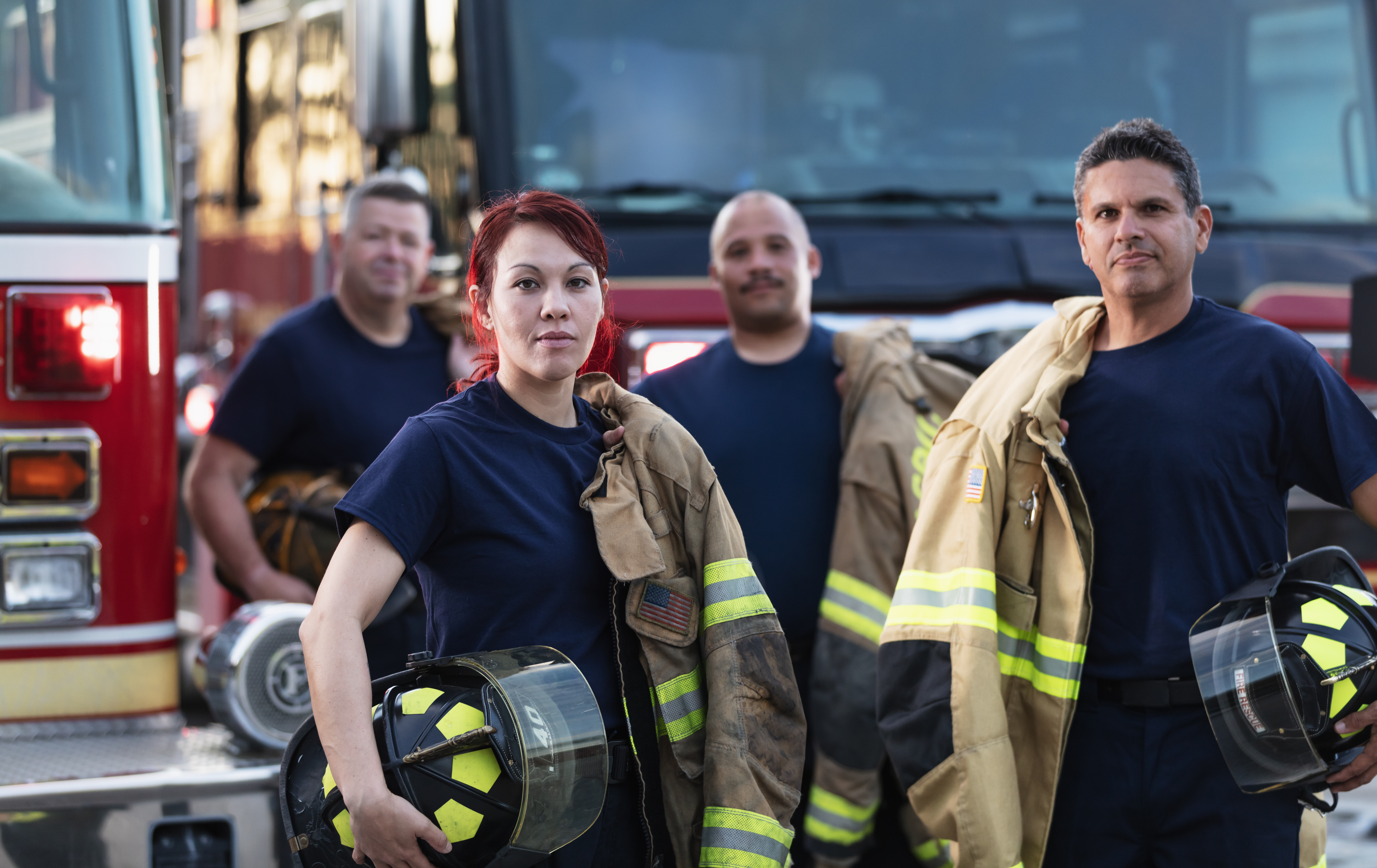 Female firefighter and group of firemen with fire trucks